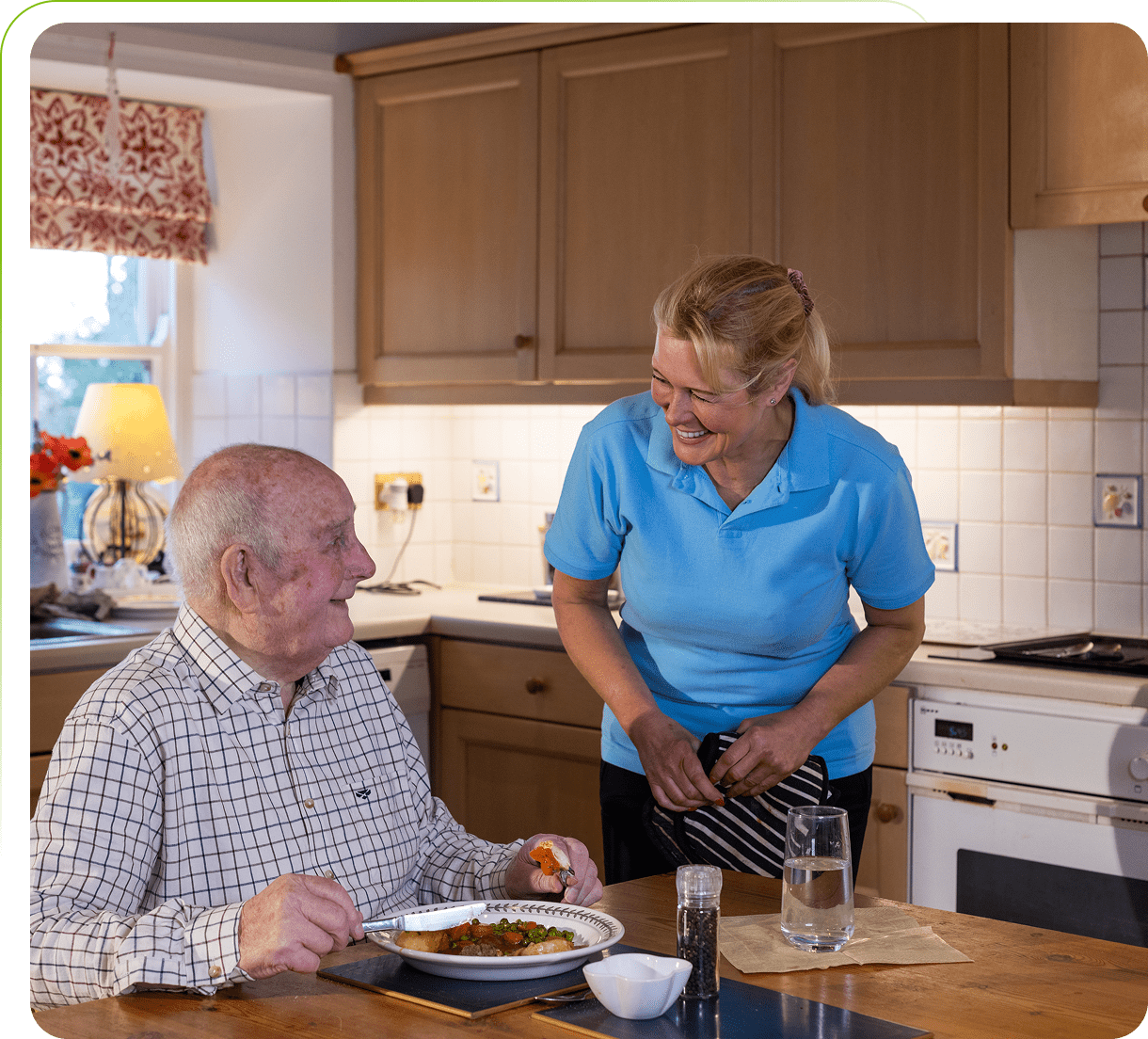 Elderly man dining with caregiver in kitchen.